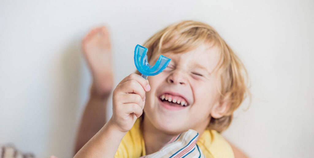 Young boy smiling while holding a blue myofunctional mouthguard